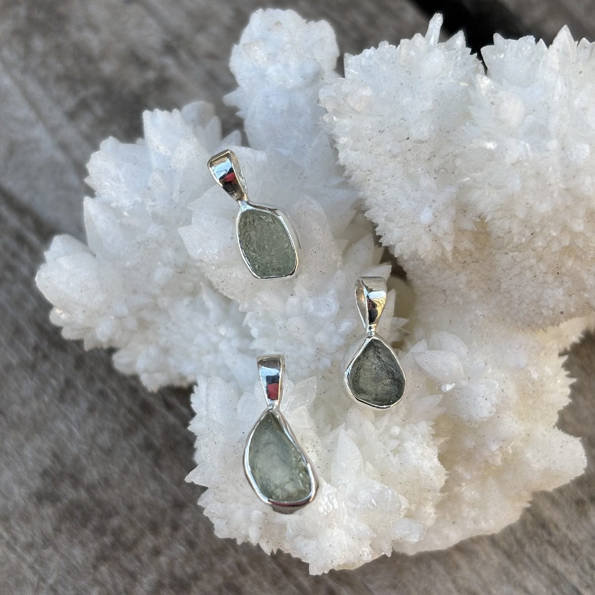 Three silver pendants with green stones on a white crystal background