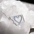Silver necklace with a heart-shaped pendant on a white stone background